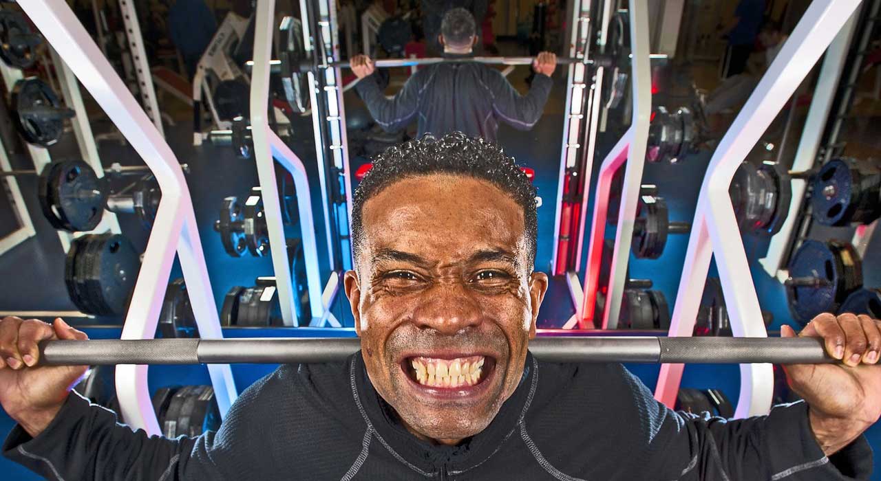 muscular man lifting a barbell on his shoulders with a grimace