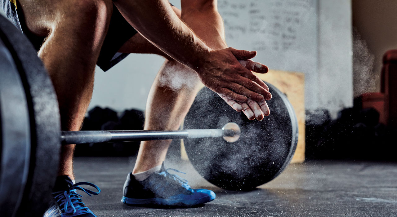 man in the gym crouched over a barbell with chalked hands