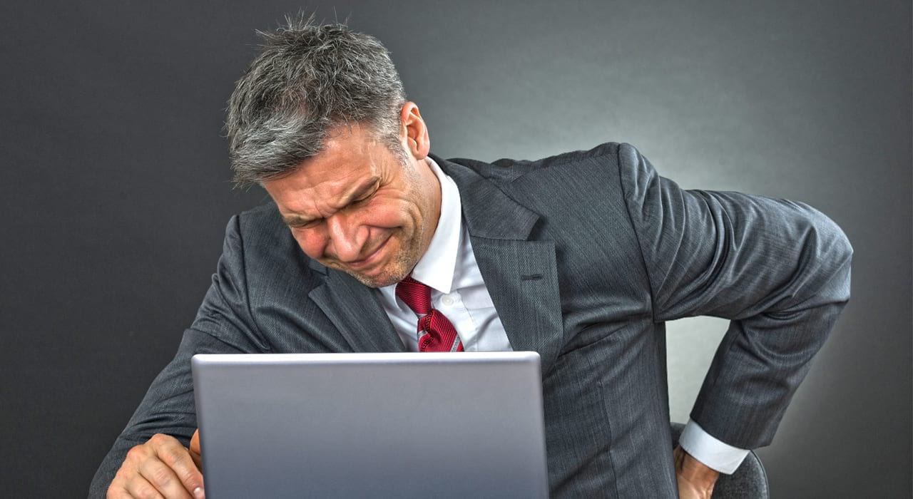man in grey suit with laptop holding his back in pain
