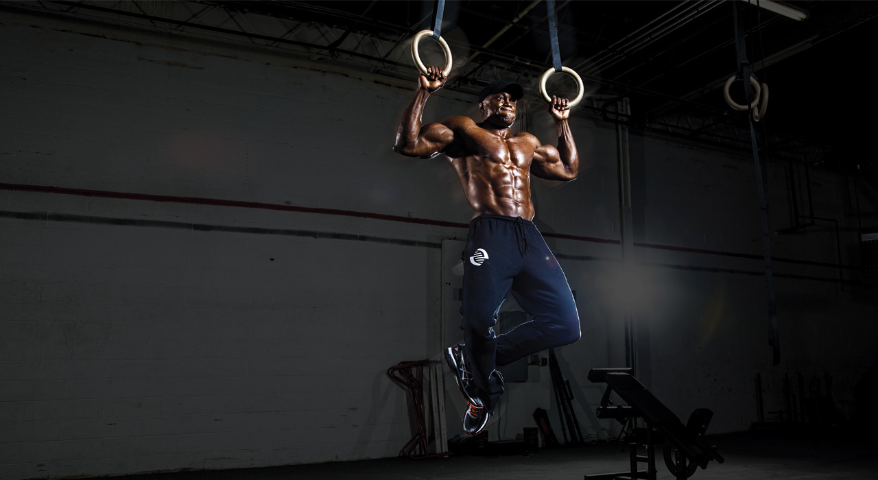 muscular man performing pull up on olympic rings