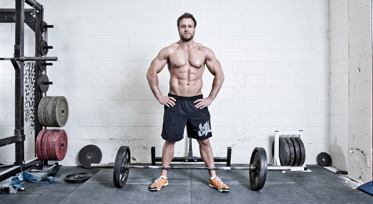 furious pete in the gym stood next to a barbell on the floor