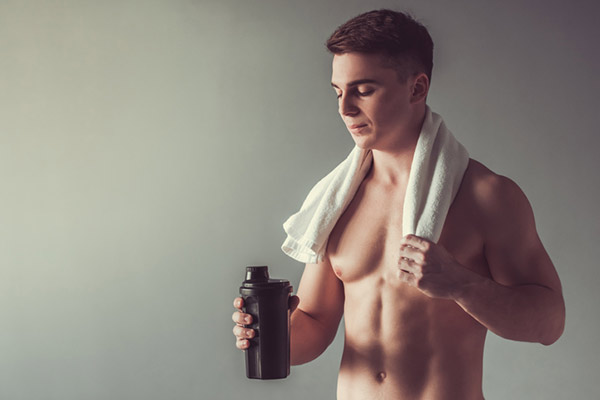 muscular man with a protein shaker and towel around their neck