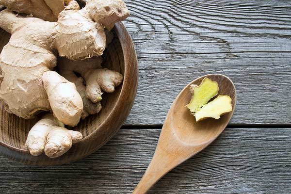 a wooden bowl filled with raw ginger and a wooden spoon with raw ginger on it
