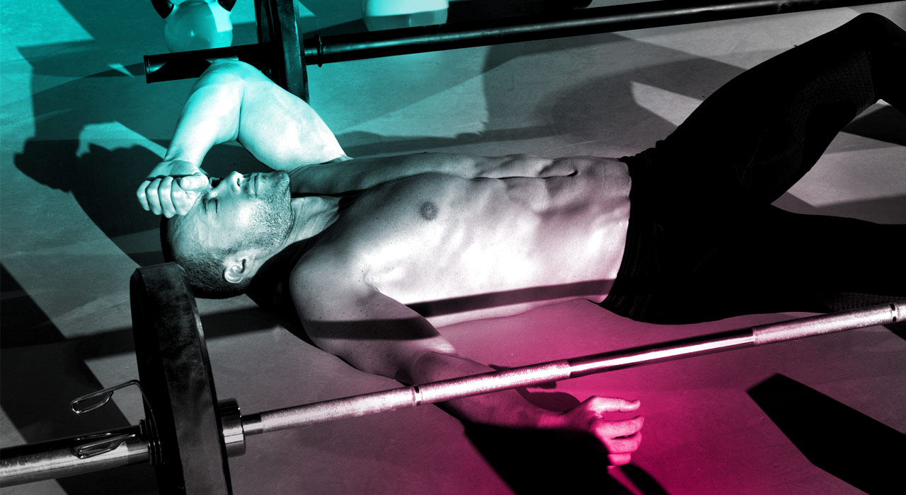 man lying down on the floor with one arm over his forehead next to a barbell