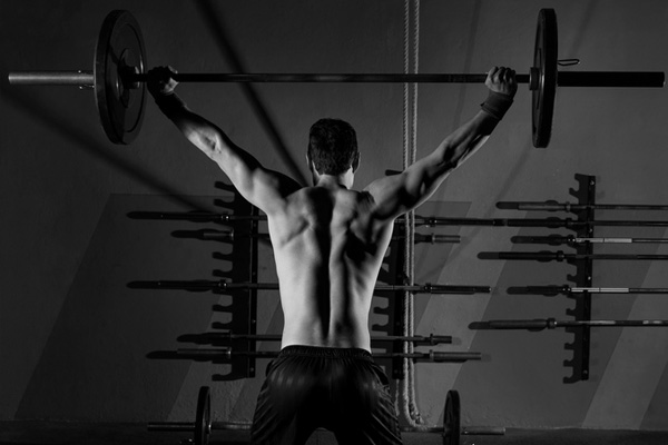 man holding barebell above his head in a gym