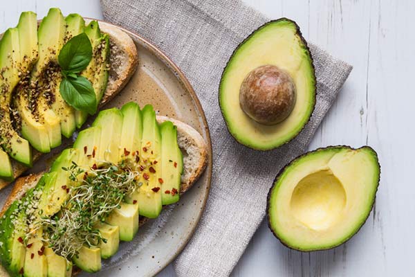 sliced avocado on toast on a plate next to two half avocados on a table