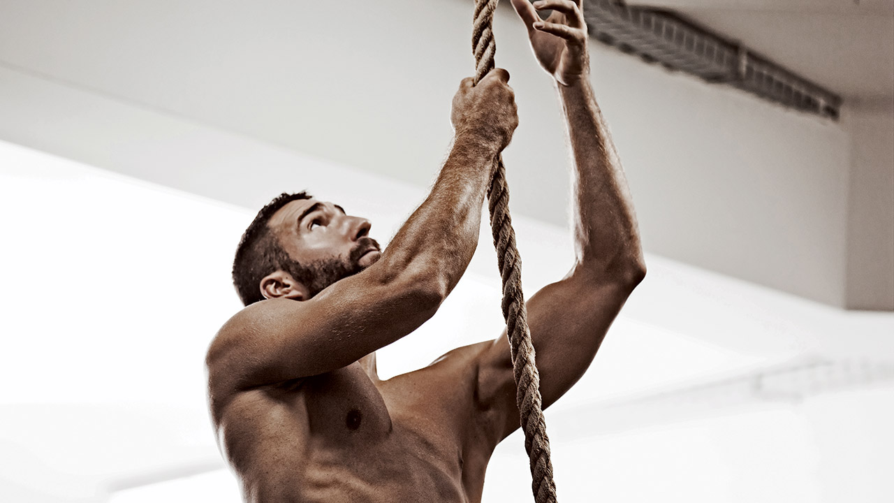 man climbing up a rope topless