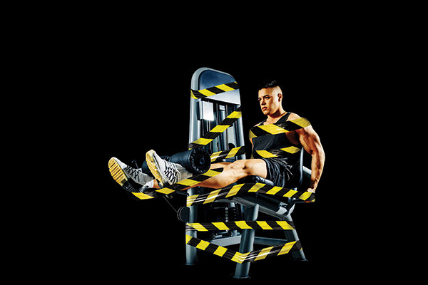 muscular man on a leg extension machine with safety tape wrapped around them