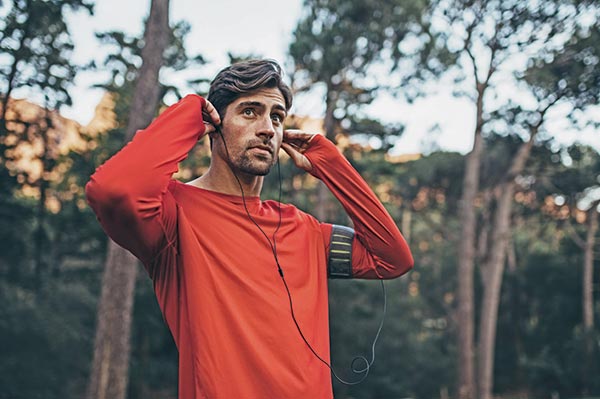 man in red long sleeved tshirt with black headphones standing in front of some trees