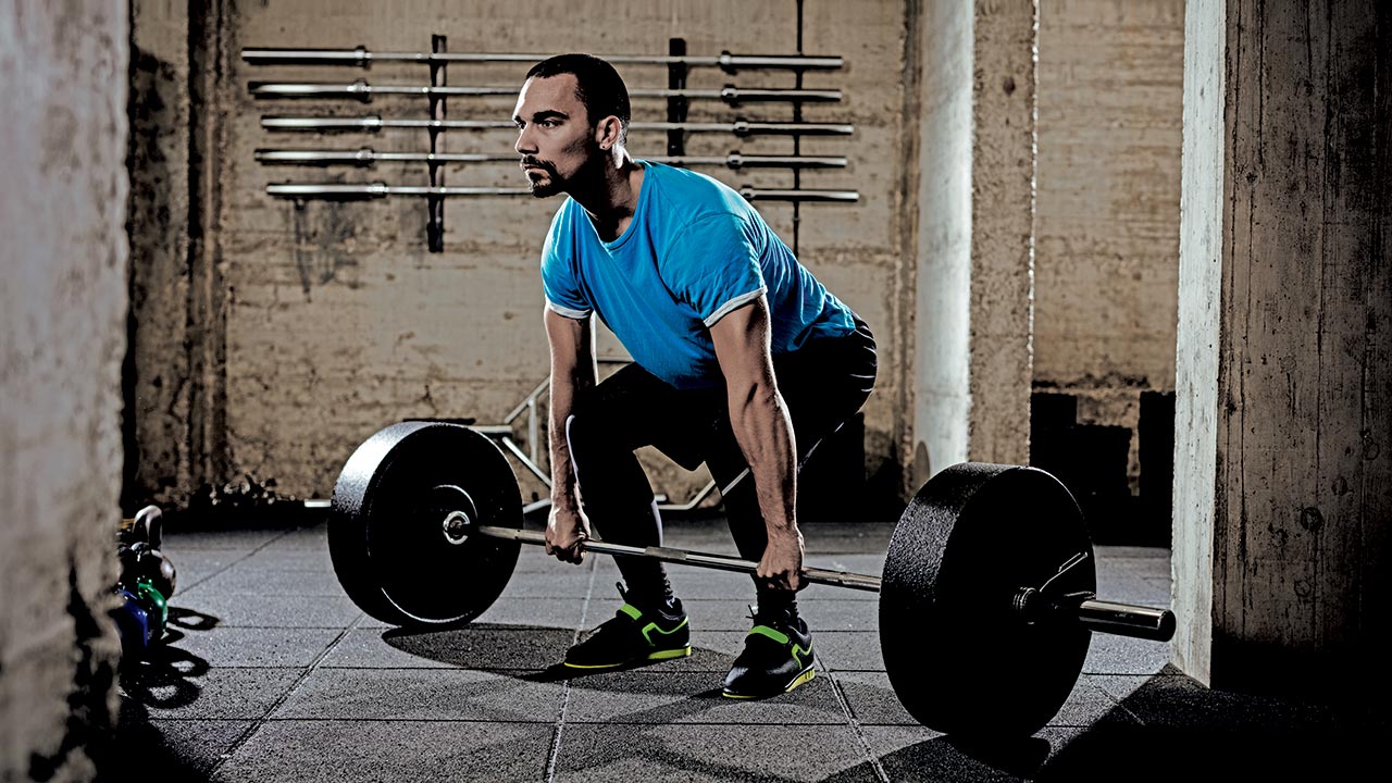 man hunched down with a barbell next to his feet