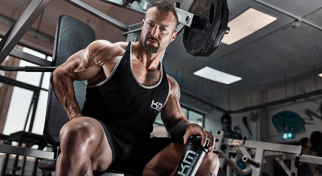 kris gething in kaged muscle attire sitting in the gym