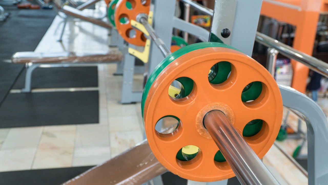 barbell with green and orange weights on a chest press bench