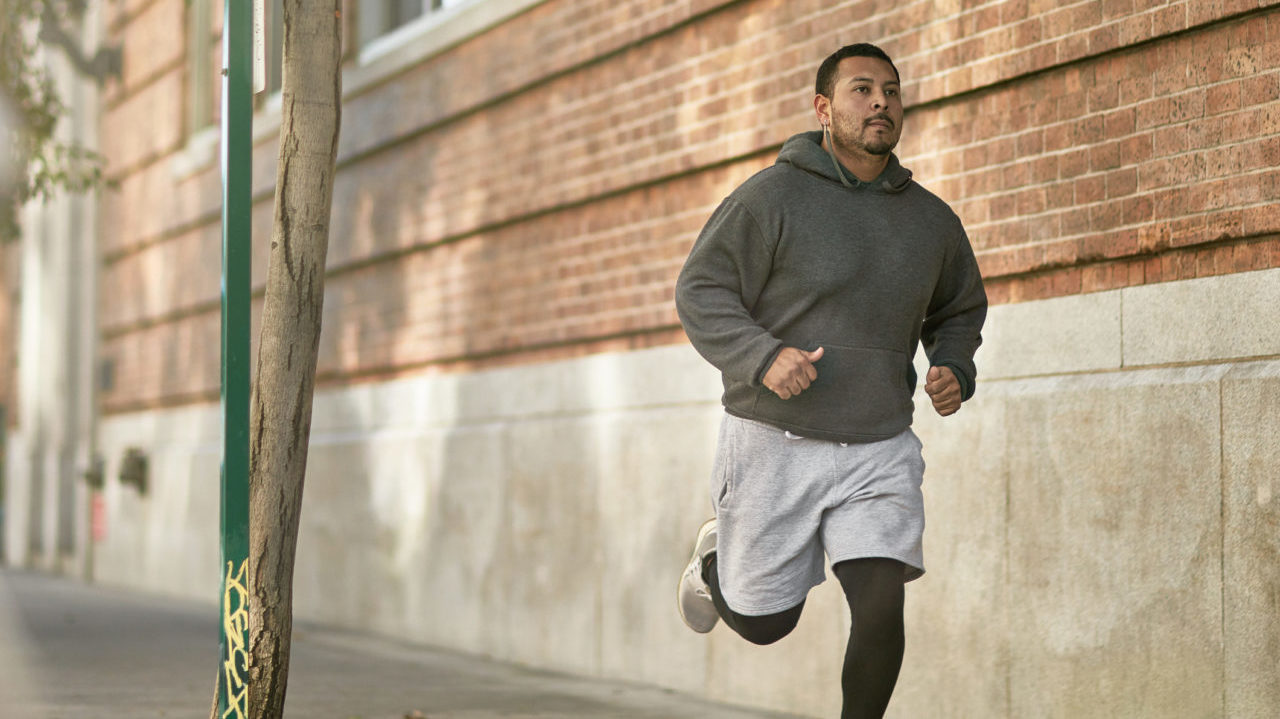 male running along the side walk with grey hoodie grey shorts