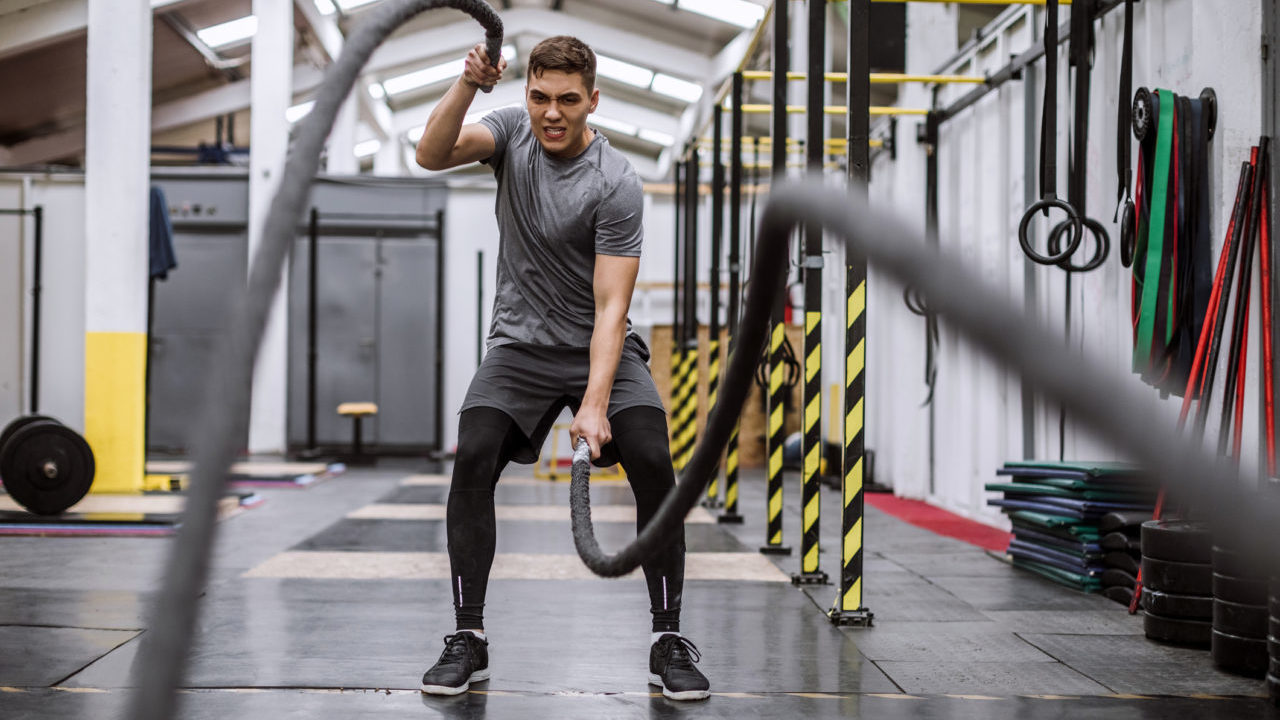 man performing battle rope exercise in a gym