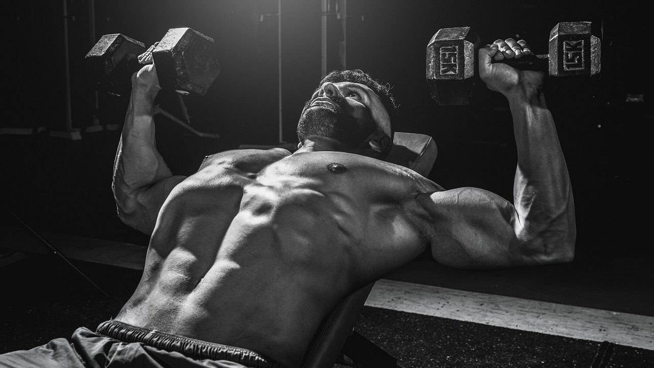 muscular man performing incline bench press with dumbbell weights